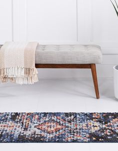 a bench sitting on top of a white floor next to a potted plant and rug