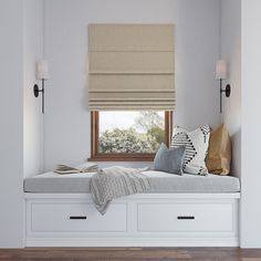 a window seat with pillows and blankets on it next to a window in a white room