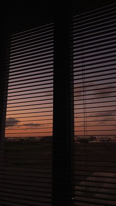 the sun is setting over an airport as seen through two windows with blind shades on them