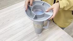 a person holding a plastic cup holder on top of a wooden table next to a white wall