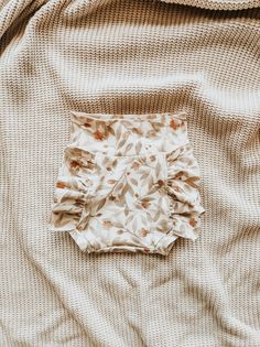 a square piece of cloth laying on top of a white bed sheet covered in brown leaves