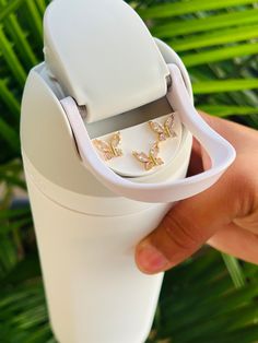 a hand holding a white cup with two butterfly rings in it's holder on top of a palm tree