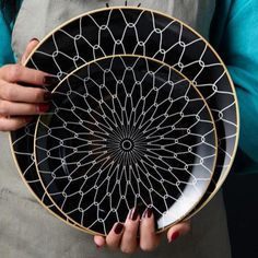 a woman holding a black and white plate with an intricate design on the front, in her hands