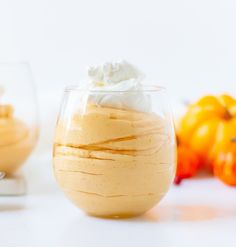 a dessert in a glass with whipped cream and pumpkins around the edges, on a white surface