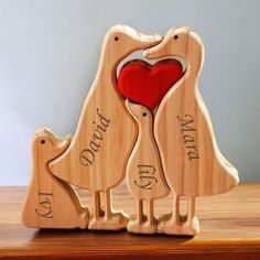 two wooden birds holding a red heart on top of a table