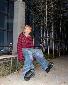 a young man sitting on a bench in front of a building at night with his eyes closed