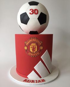 there is a soccer ball sitting on top of a red and white cake that says manchester united