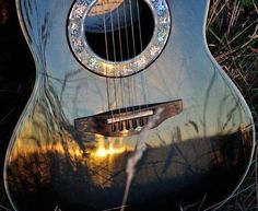 an acoustic guitar sitting in the grass with its reflection on it's back end