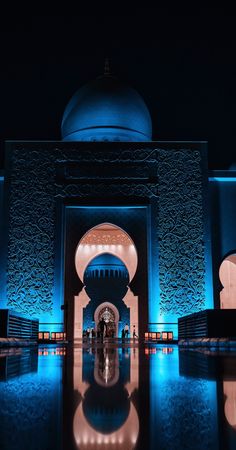 the entrance to an ornate building lit up with blue lights and mirrors on the floor