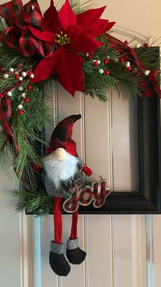 a christmas wreath with a gnome and poinsetti hanging on the front door frame