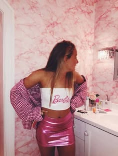 a woman standing in front of a bathroom mirror wearing a pink skirt and crop top