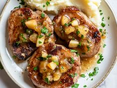 two pork chops with potatoes and gravy on a white plate next to mashed potatoes