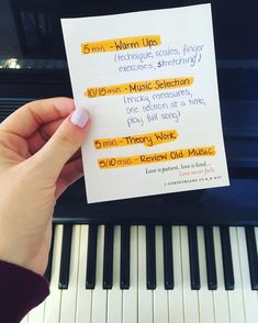 someone holding up a piece of paper with writing on it next to a piano keyboard