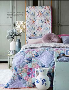 a bed with a quilted headboard and pillows on it, next to a vase