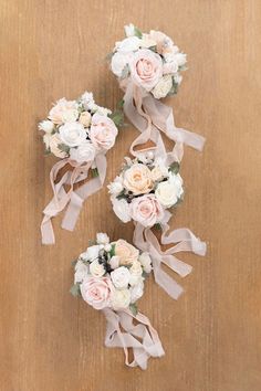 three bridal bouquets with pink and white flowers are arranged on a wooden surface