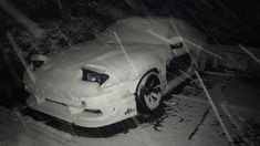 a car covered in snow parked on the side of a road at night with it's hood up