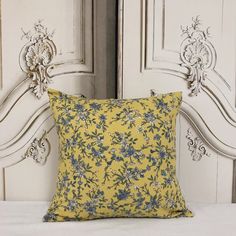 a yellow and blue pillow sitting on top of a white bed next to a wooden headboard