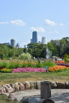 a man sitting on a bench in a park with flowers and buildings in the background