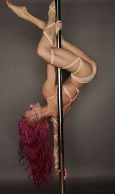 a woman with red hair is on the pole and has her legs bent over it