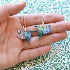 two tiny hummingbirds sitting on top of each other's fingers in front of a hand