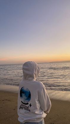 a person standing on top of a beach near the ocean with a hoodie over their head