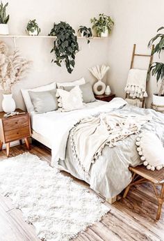 a bed with white sheets and pillows in a bedroom next to two potted plants