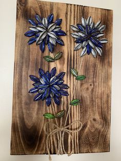 three blue and white flowers are on a wooden board with string attached to it,