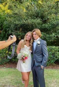 a man and woman posing for a photo in front of some bushes with their cameras