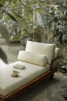 an outdoor chaise lounge with pillows and a cup sitting on it's side