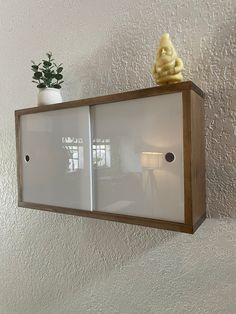 a white cabinet with two glass doors and a small buddha statue on the top shelf