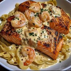 some salmon and shrimp are on top of pasta in a white bowl with lemon sauce