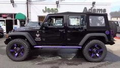 a black jeep is parked in front of a jeep dealership with purple rims