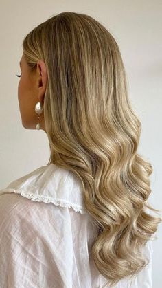 a woman with long blonde hair wearing a white blouse and pearl earrings, looking off to the side