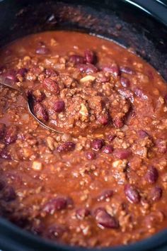 a spoon is in a slow cooker filled with chili and beans, ready to be eaten