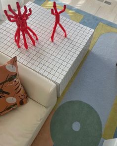 two red plastic figures sitting on top of a white couch next to a blue and yellow rug