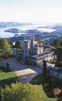 an aerial view of a large mansion in the middle of a lush green field with mountains in the background