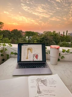 an open laptop computer sitting on top of a table next to a cup and book