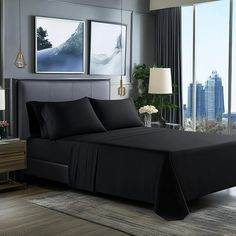 a bed with black sheets and pillows in a bedroom next to a window overlooking the city