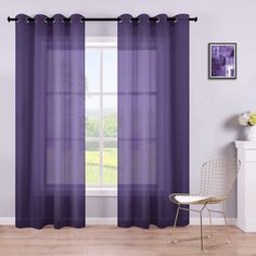 a purple curtain hanging in front of a window with a white chair next to it