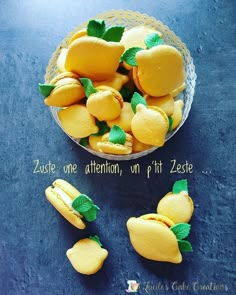 a bowl filled with lemons on top of a blue table next to green leaves