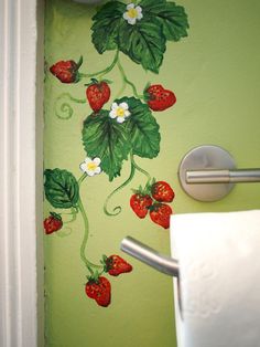 a green wall with strawberries painted on it and a toilet paper dispenser