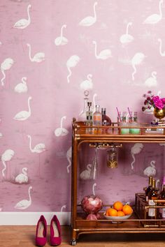 a pink wall with flamingos painted on it and some bottles in front of the shelf