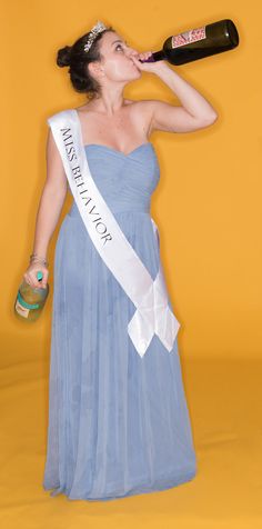 a woman in a blue dress drinking from a wine bottle with a ribbon around her neck