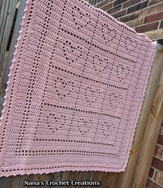 a pink crocheted blanket hanging on a wooden fence next to a brick wall