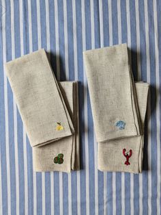 three pieces of linen with embroidered designs on them sitting on a striped table cloth,