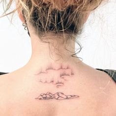 a woman's back neck with a cloud and mountains tattoo on her left side