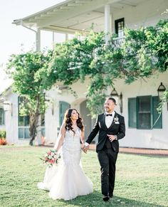 a bride and groom holding hands in front of a house