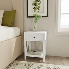 a bedroom with a bed and a white nightstand next to a plant in a vase