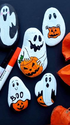 painted rocks with ghost faces and pumpkins on them, next to an orange marker