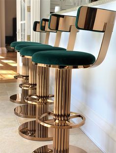 three gold barstools with green velvet seats in front of a white kitchen counter